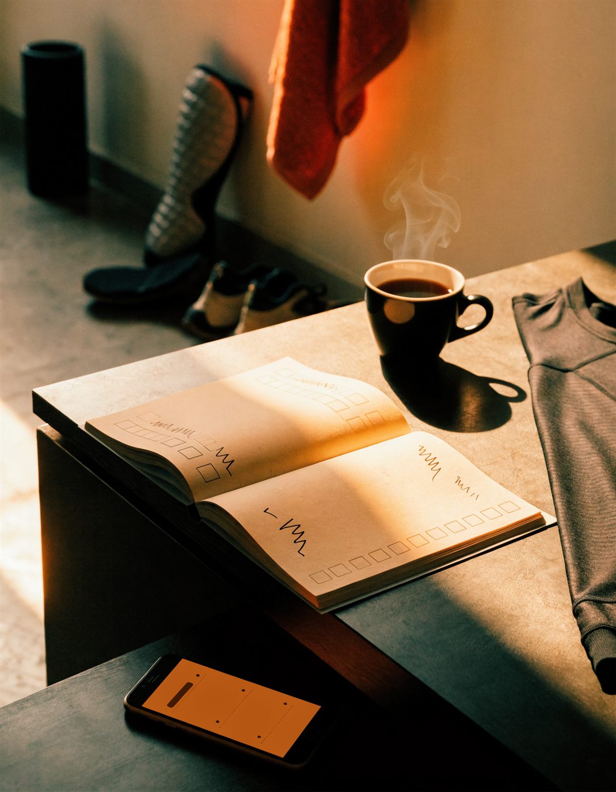 Open paper planner, steaming coffee, and folded training gear on a desk before sunrise
