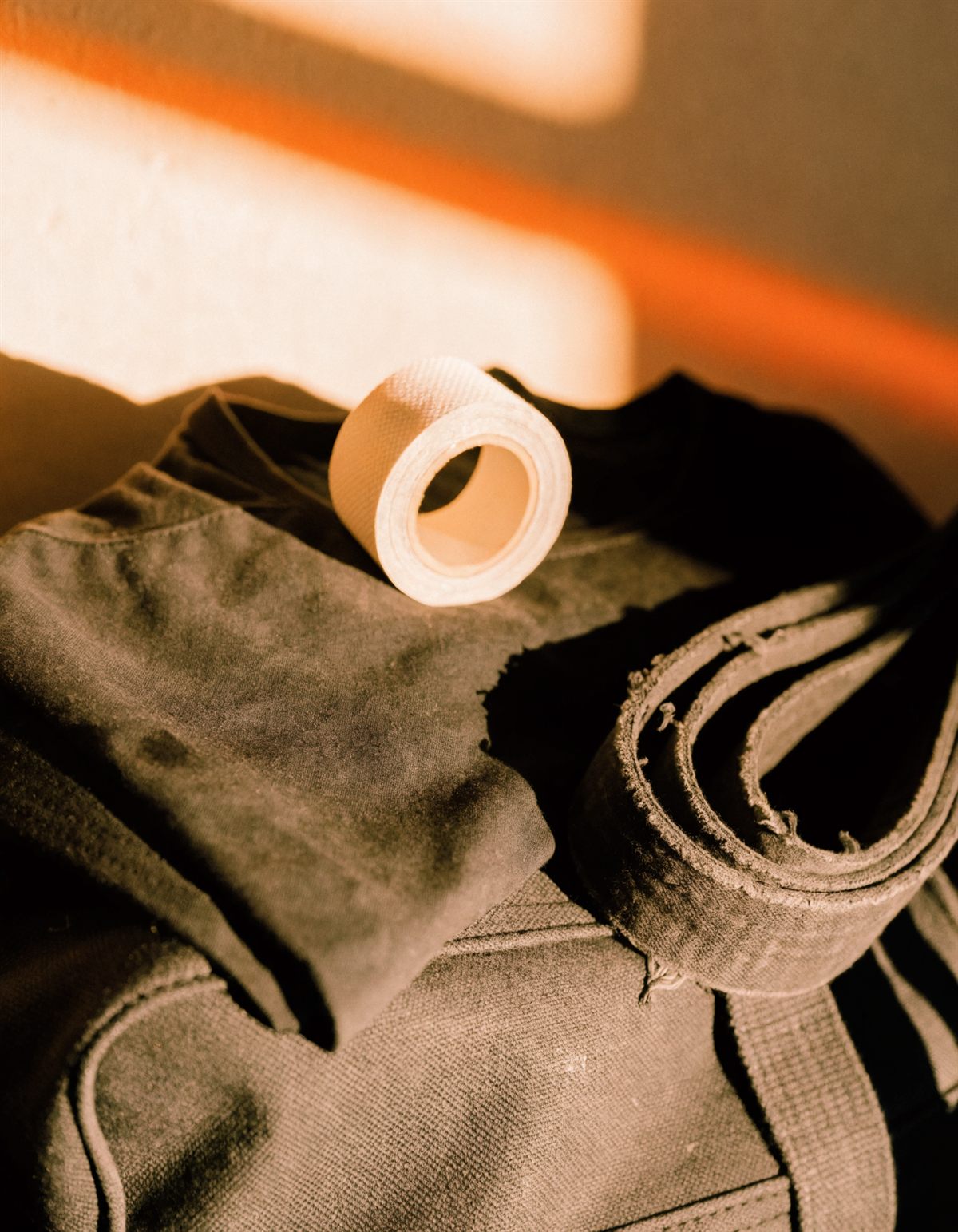 Folded black training shirt with a worn belt, finger tape, and a canvas gym bag in low morning light